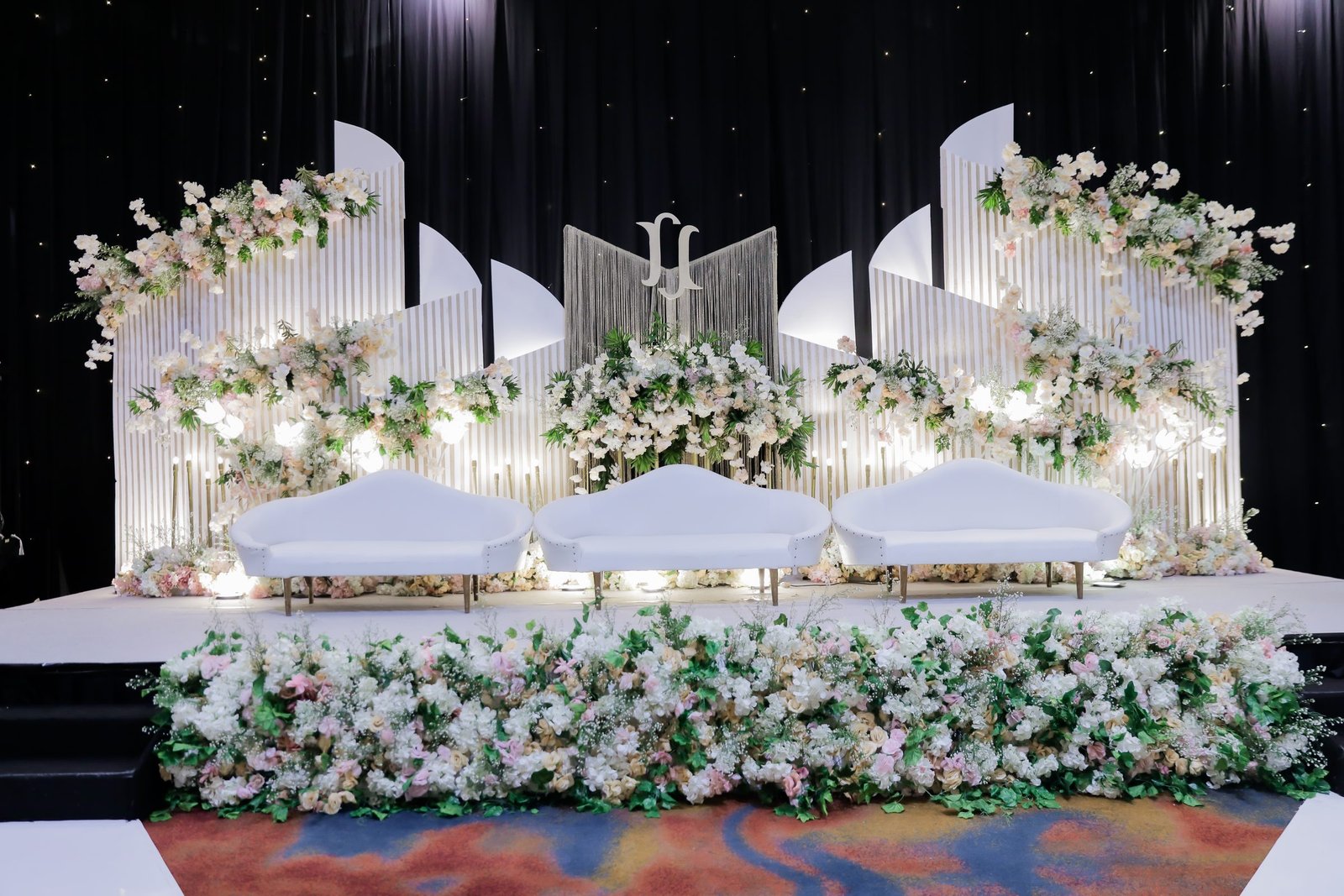 Sculptural ivory stage backdrop with cascading blush and white floral arrangements and gold monogram, built by Aluna's Pavilion