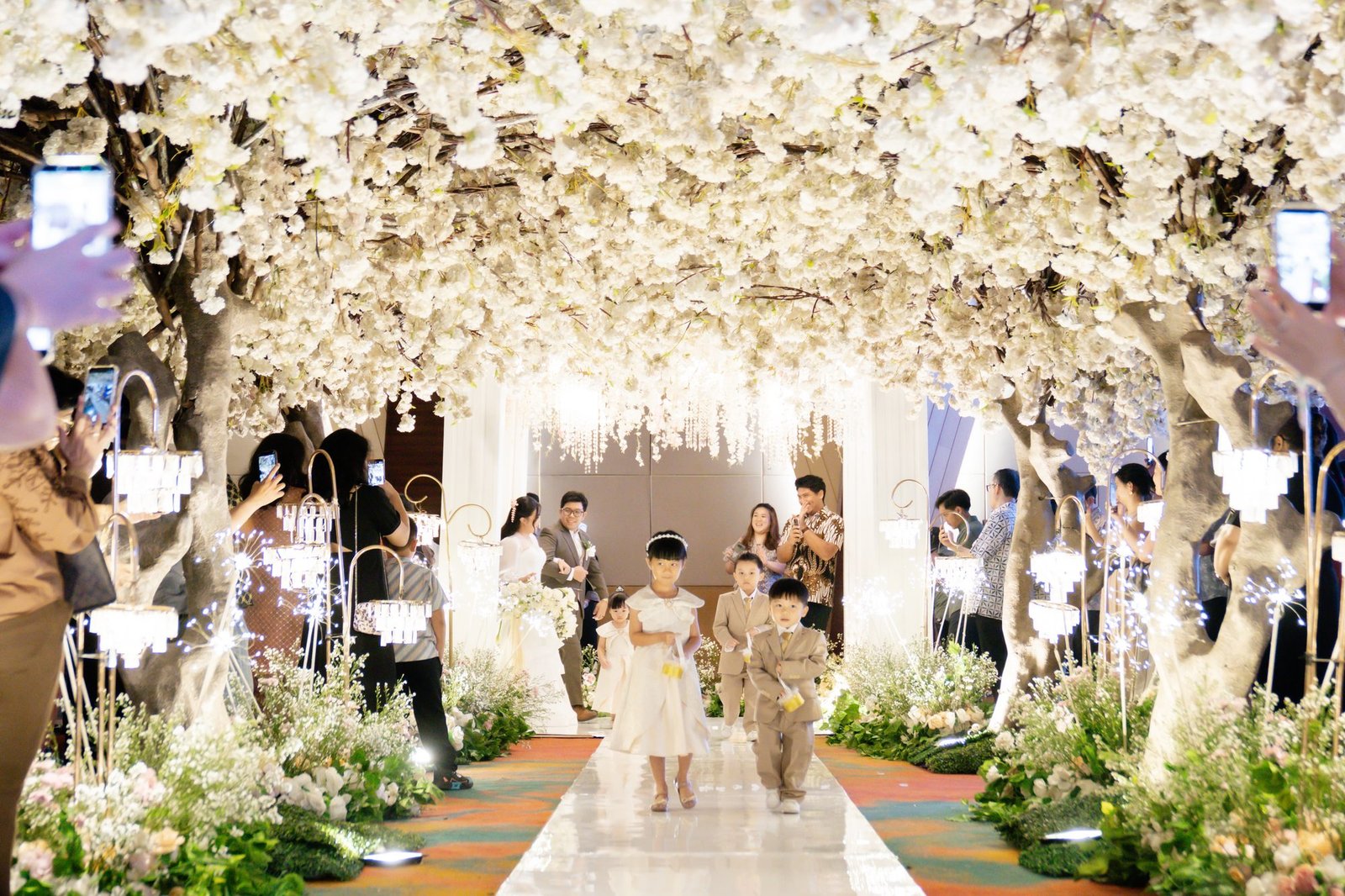 Flower girl and ring bearer walking down a petal aisle beneath a white blossom canopy at an Aluna's Pavilion wedding