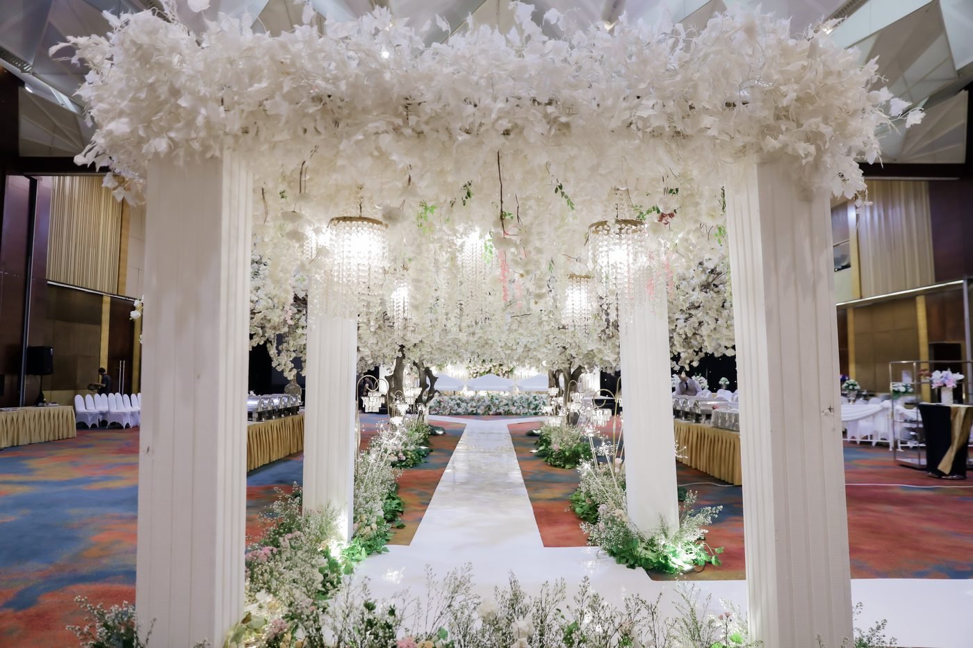 White floral pergola with columns and hanging crystal chandeliers over the aisle