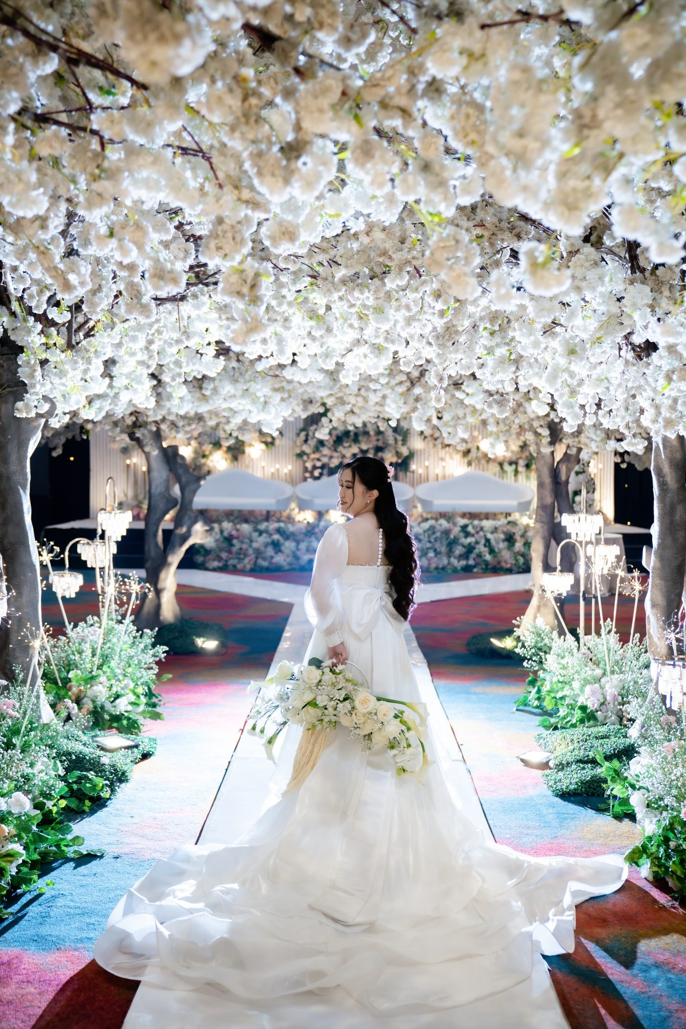 Bride viewed from behind walking beneath a white blossom canopy